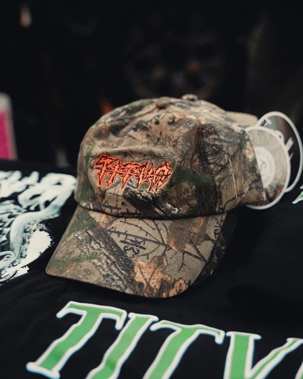 Camo baseball cap with fiery red logo displayed on black cloth.