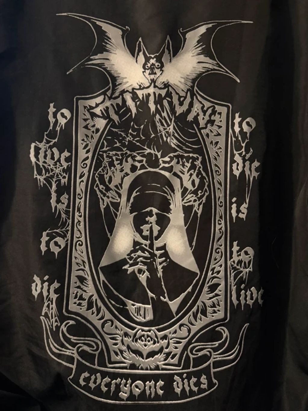 Gothic design with a nun, bat, and skulls saying 'to die is to live, everyone dies'.