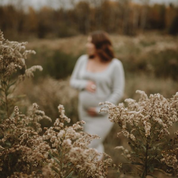 Pregnant woman in a serene field with soft focus.