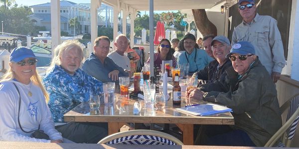 Group of people enjoying drinks at an outdoor table on a sunny day.