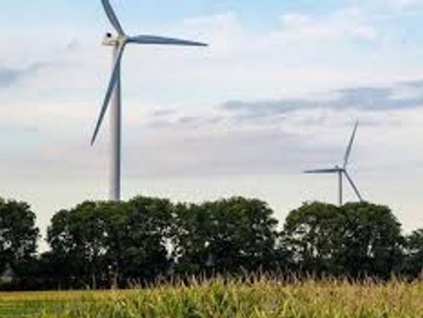 Wind turbines standing tall above green trees and fields under a partly cloudy sky.
