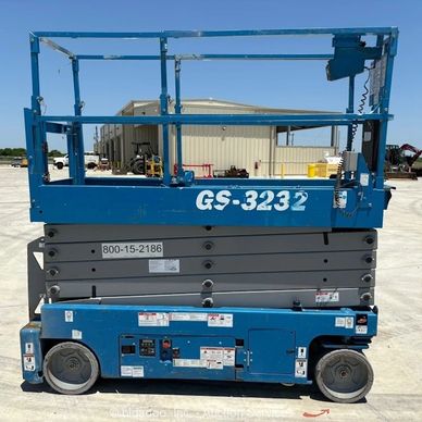 Blue scissor lift in an outdoor industrial area.