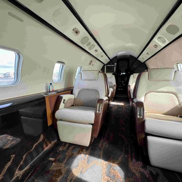 Luxurious seats inside a private jet with ample legroom and large windows.