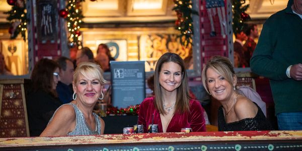 Three women smiling at a festive holiday gathering indoors.