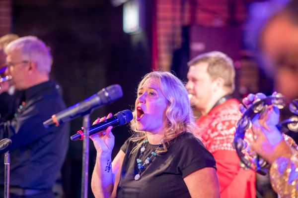 Woman passionately singing with band in vibrant stage lighting.
