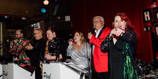 A lively band with multiple singers performing on stage in colorful outfits.