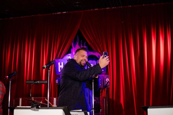Man taking a selfie on stage with red curtains in the background.
