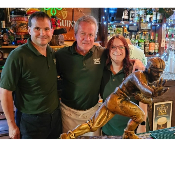 Three people smiling behind a football player statue in a bar.