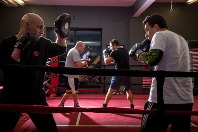 Two pairs of men training in a boxing gym with focus pads and gloves.