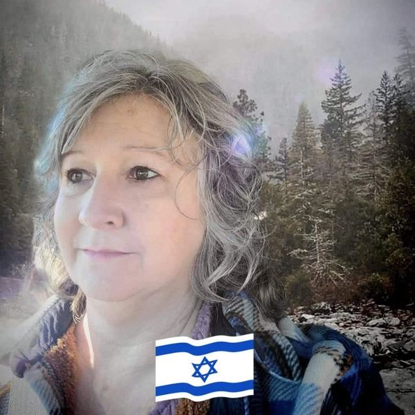 A woman with gray hair outdoors in a forested area with an Israeli flag overlay.