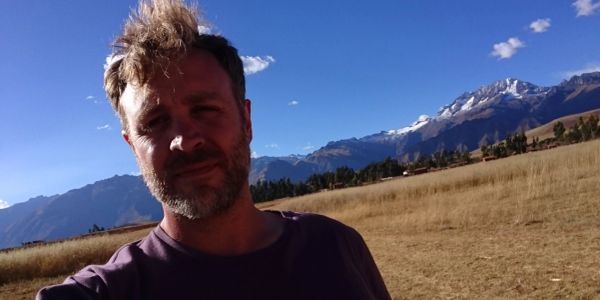 Man taking a selfie in a sunny mountainous field.