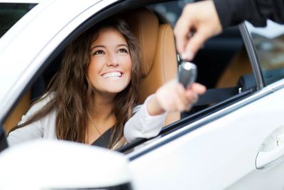Smiling woman in a car receiving keys from another person