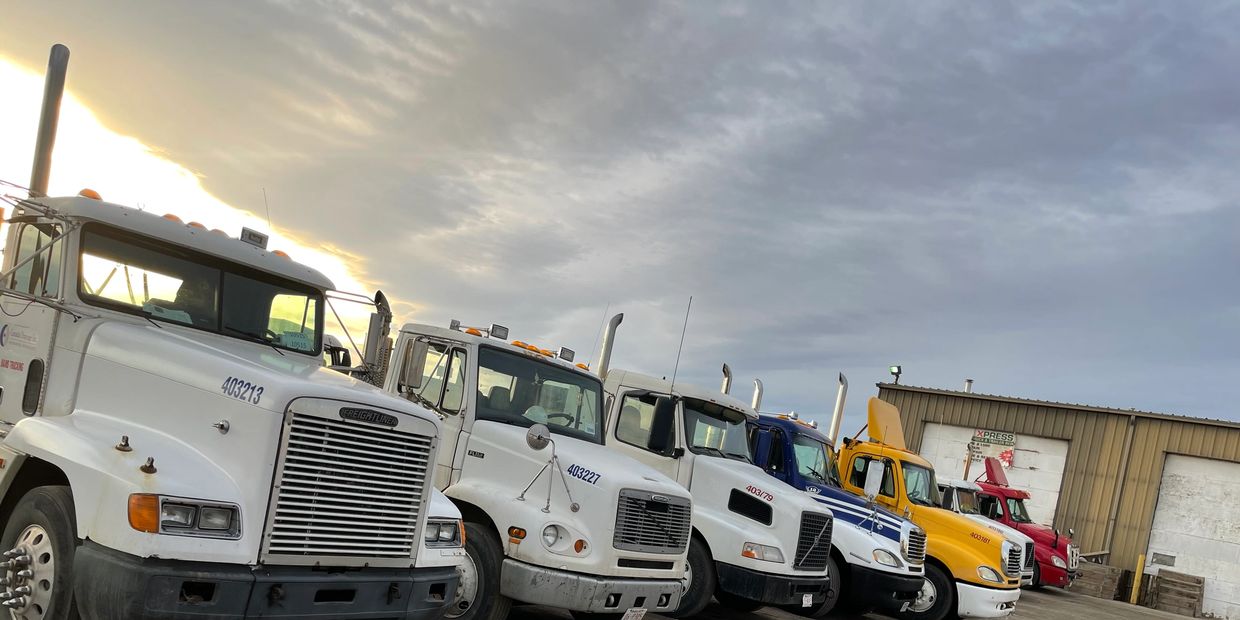 A lineup of colorful semi trucks parked outside a warehouse under a cloudy sky.