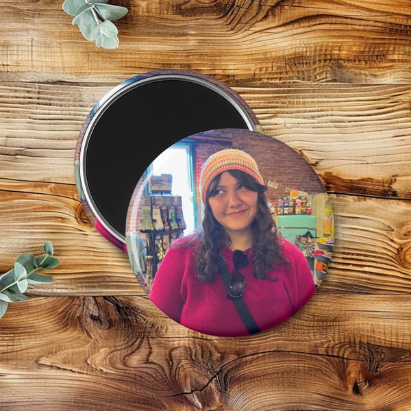 Round photo magnet with a smiling woman in a colorful beanie and pink sweater.