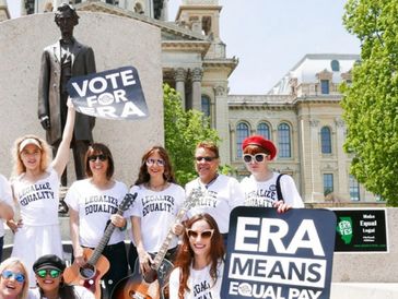 Group advocating for ERA and equal pay with signs and guitars.