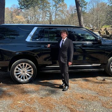 Man in suit standing next to a black luxury SUV outdoors.