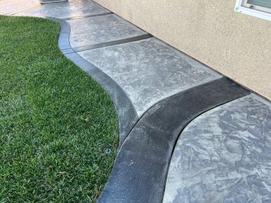 Decorative curved concrete sidewalk beside grass and a house wall.