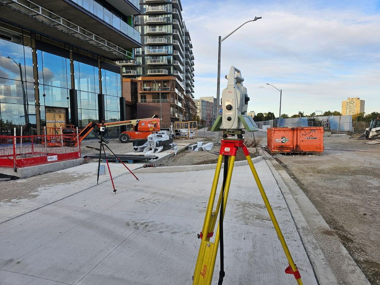 Total station on a yellow tripod beside a high-rise building under construction.