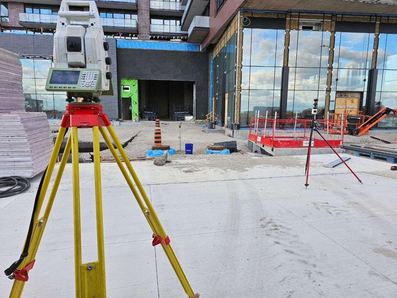 Total station on a yellow tripod in front of a building entrance under construction.