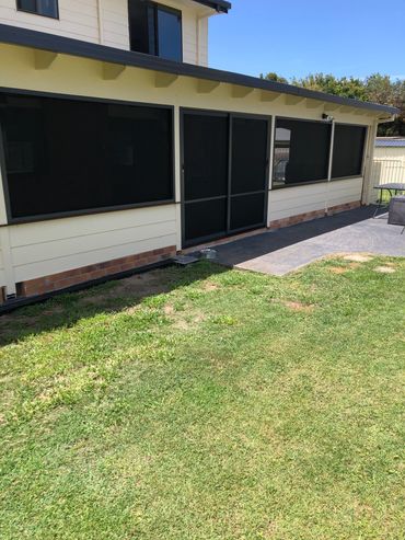 Backyard with green lawn and a house patio with screened windows.