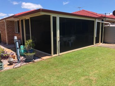 Backyard patio enclosed with dark mesh screens beside a red-roofed house.