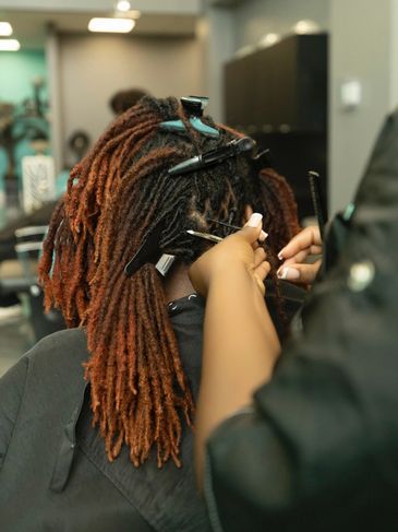 Person getting their dreadlocks styled with clips and tools.