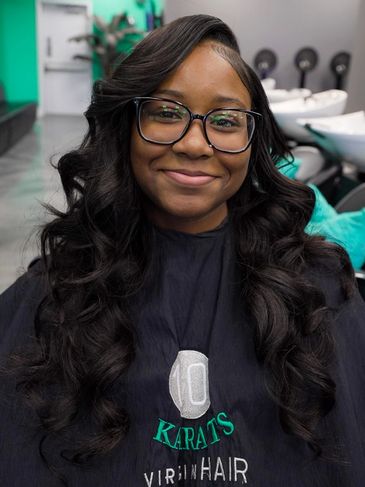 Smiling woman with long, styled hair and glasses in a salon.