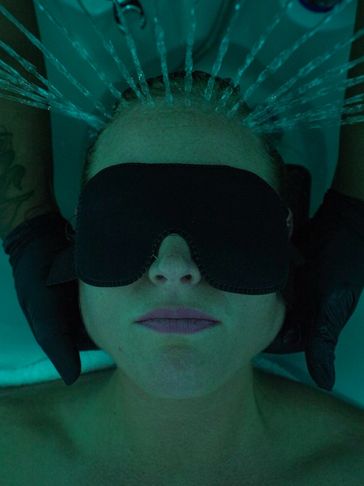 Person wearing a blindfold receiving a water treatment on their head.