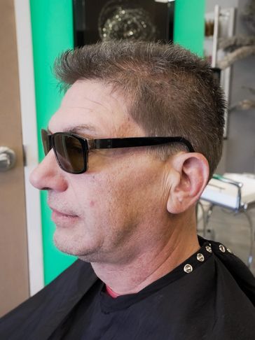 Side profile of a man wearing sunglasses in a barber's chair.