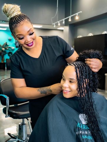 A hairdresser smiles while braiding a client's hair in a salon.