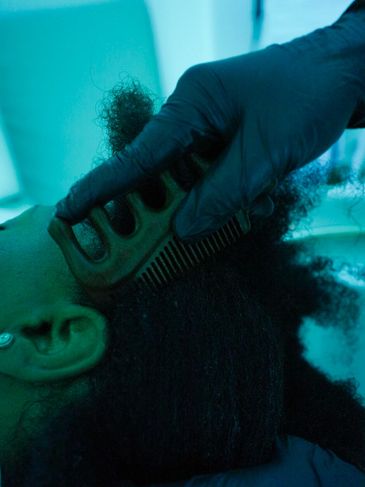A gloved hand combing a person's curly hair.