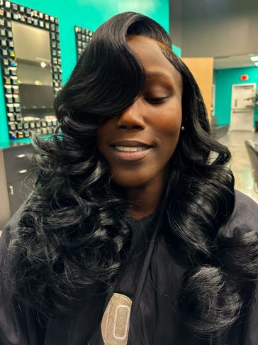 Woman with glossy, voluminous black curls smiles with eyes closed in salon.