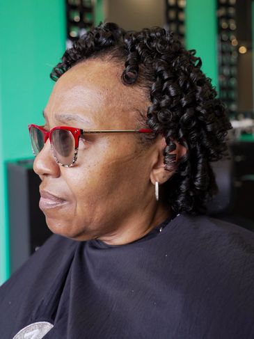 Woman with tight, glossy curls and stylish glasses.