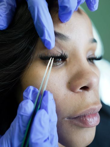 Close-up of eyelash extension application with gloves and tweezers.