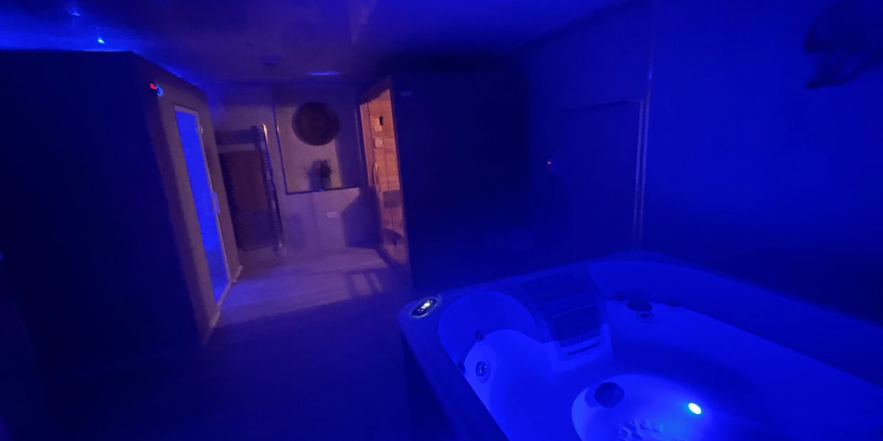 Dimly lit spa room with jacuzzi and ambient blue lighting.
