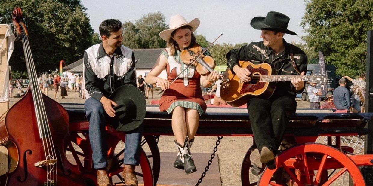 Three musicians in cowboy attire playing instruments outdoors.