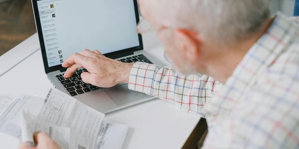 Elderly man managing finances on a laptop while holding receipts.