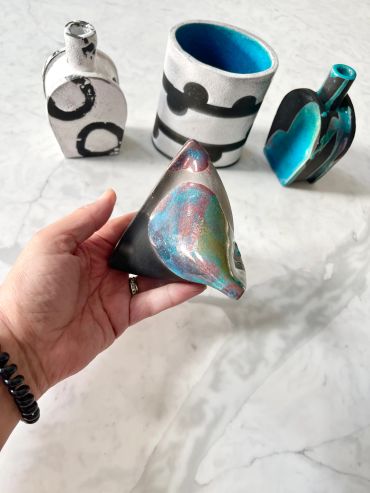 Hand holding a colorful, twisted art piece with three other decorative objects in the background.