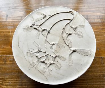Ceramic plate with botanical imprint on wooden table.