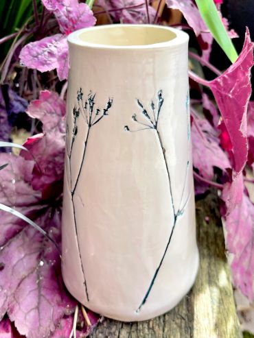 Ceramic vase with delicate floral design among pink leaves.