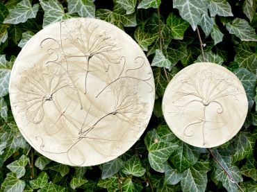 Two round plaques with flower designs against ivy leaves.