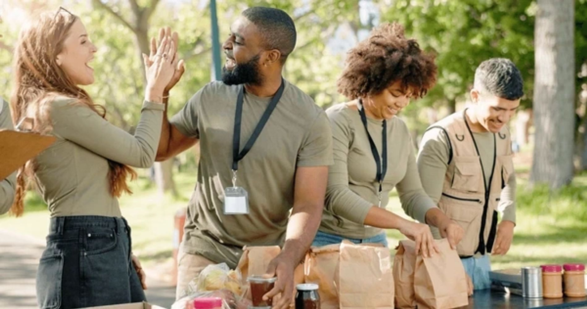 Volunteers joyfully preparing food packages outdoors, sharing a high-five.
