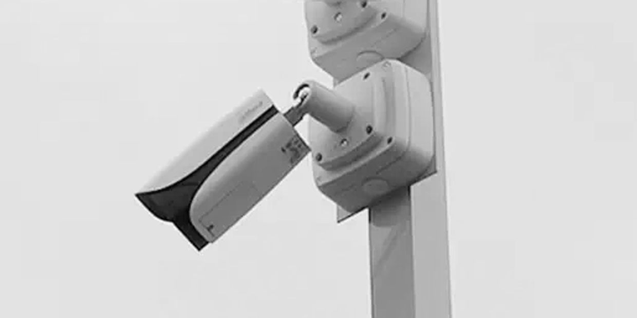 A white security camera mounted on a pole against a clear sky.