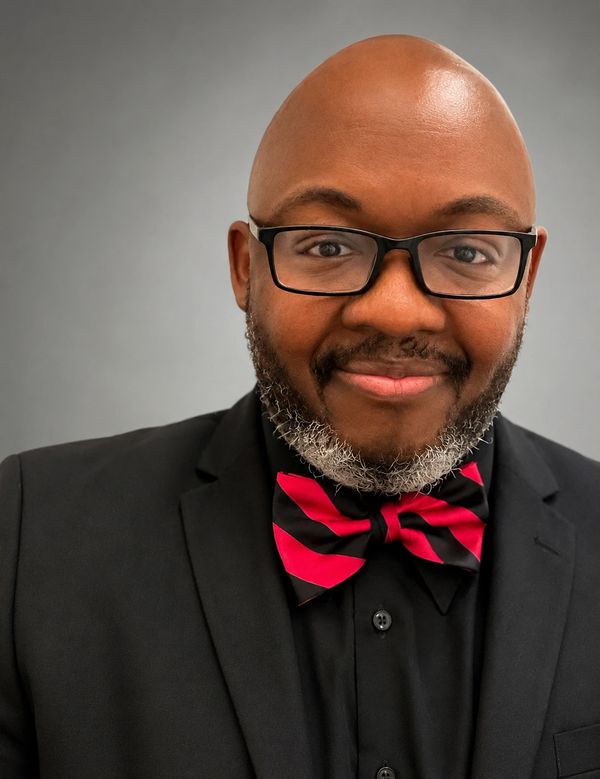 Man in glasses and a black suit with a red and black striped bow tie.