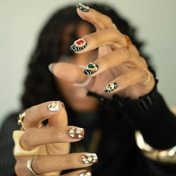 Close-up of hands with elaborate, gem-adorned nail art and rings.
