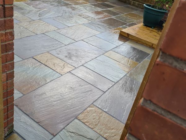 Wet, multicolored stone patio with a wooden step and potted plants.
