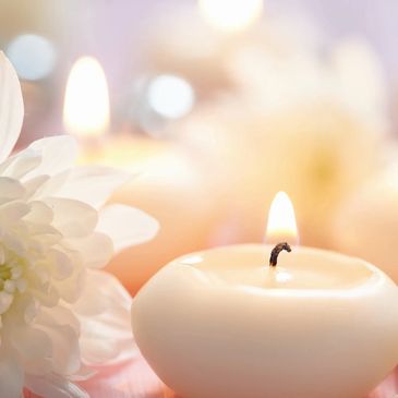 White chrysanthemum with a small white candle, which has been lit, on its left-hand side.