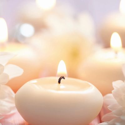 White chrysanthemum with a small white candle, which has been lit, on its left-hand side.