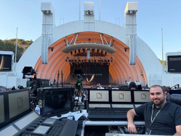 Man sitting at a control station in front of an outdoor stage.