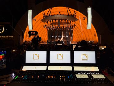 Concert stage with control panels and orange backdrop.
